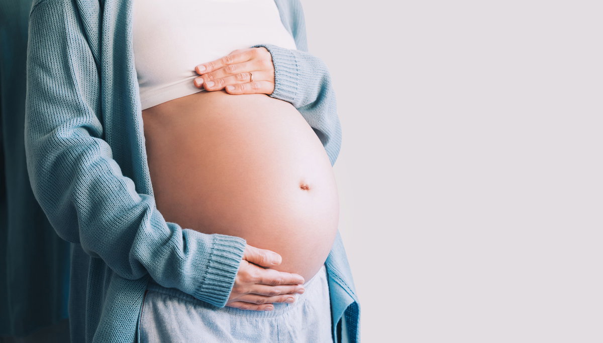 Schwangere Frau hält sich glücklich den Bauch.
